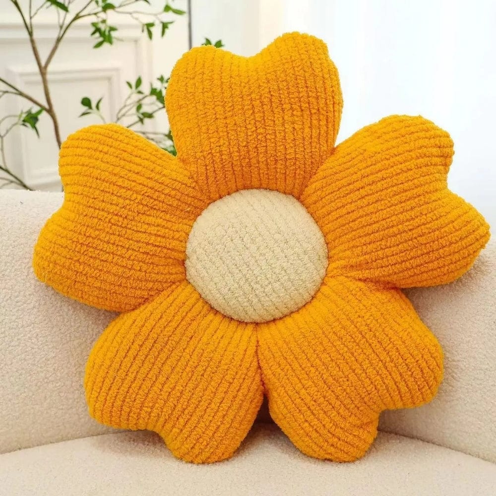 Coussin décoratif en forme de fleur, avec des pétales orange et un centre beige, posé sur une banquette