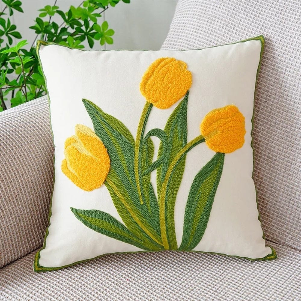 Coussin décoratif avec des tulipes jaunes brodées sur fond blanc, posé sur un canapé en tissu