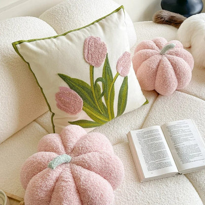 Coussin décoratif beige avec des tulipes roses, posé sur un canapé blanc, entouré de coussins en forme de citrouille