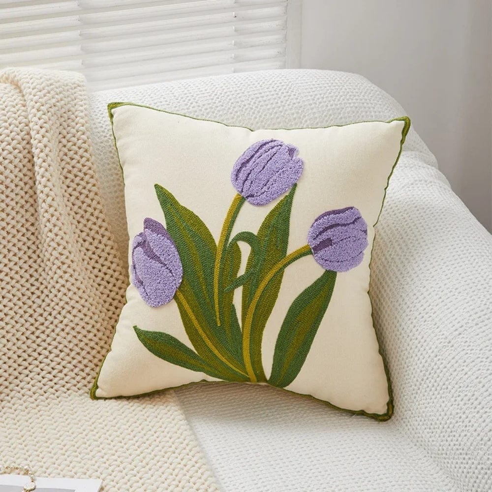Coussin décoratif avec des tulipes violettes sur fond crème, posé sur un canapé texturé