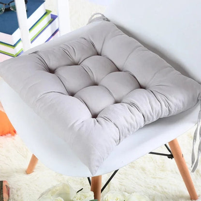 Coussin déco carré en tissu gris clair, rembourré avec un motif matelassé, posé sur une chaise moderne