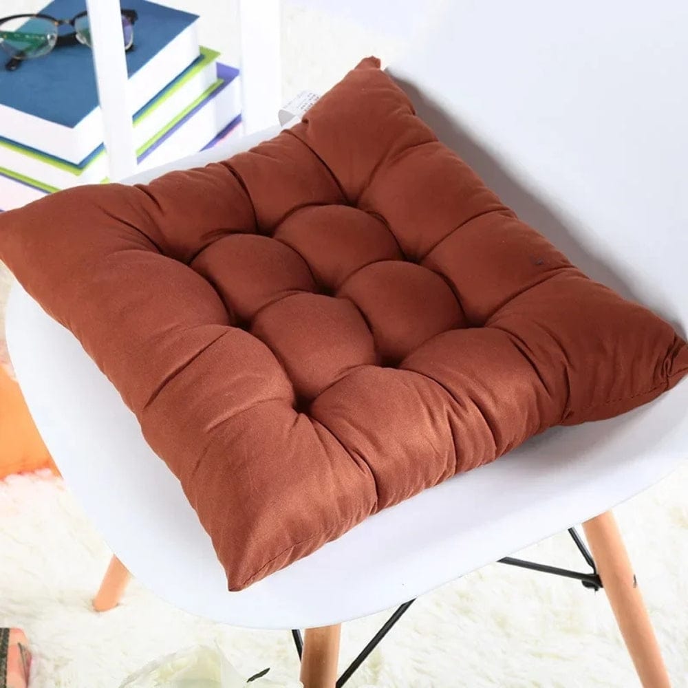Coussin déco en tissu marron, matelassé, posé sur une chaise blanche dans un salon lumineux