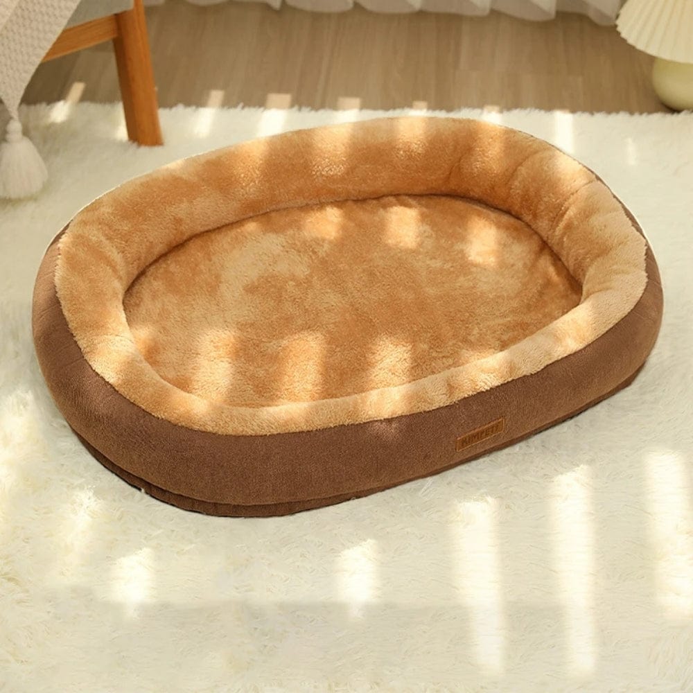 Coussin de forme ovale en tissu doux beige et marron, posé sur un tapis moelleux dans un salon lumineux