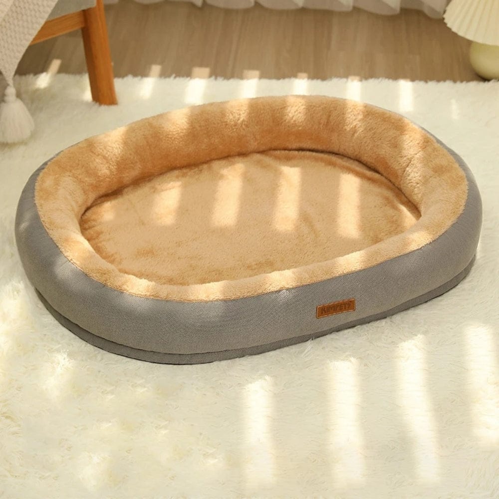 Coussin de chat oval en tissu gris avec intérieur en peluche beige, posé sur un tapis doux dans un salon