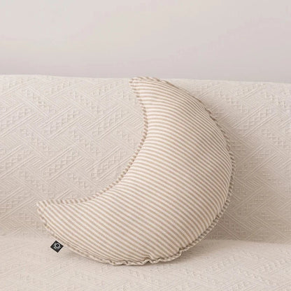 Coussin décoratif en forme de croissant, rayé beige et blanc, posé sur un canapé clair