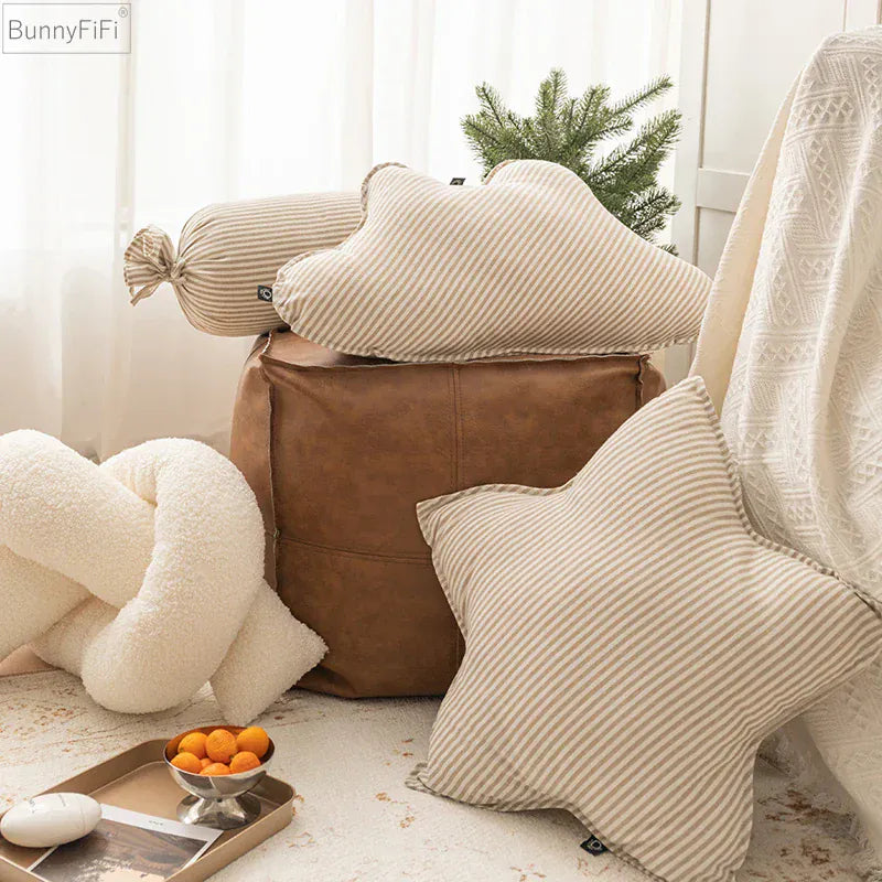 Coussins décoratifs à rayures beige et crème disposés sur un pouf en cuir dans un salon lumineux