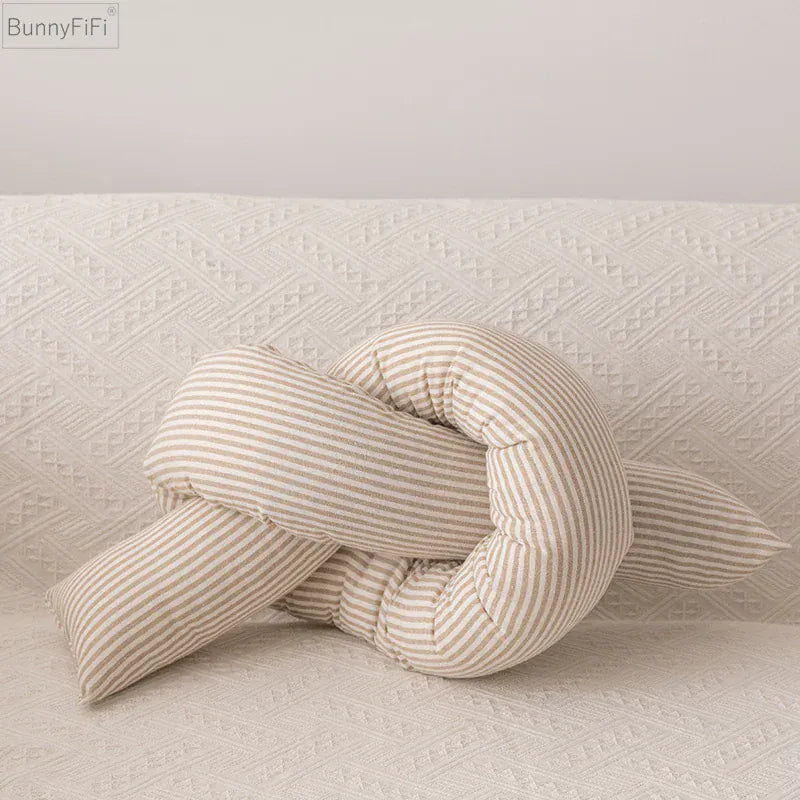 Coussin décoratif en forme de nœud, rayé beige et blanc, posé sur un canapé texturé