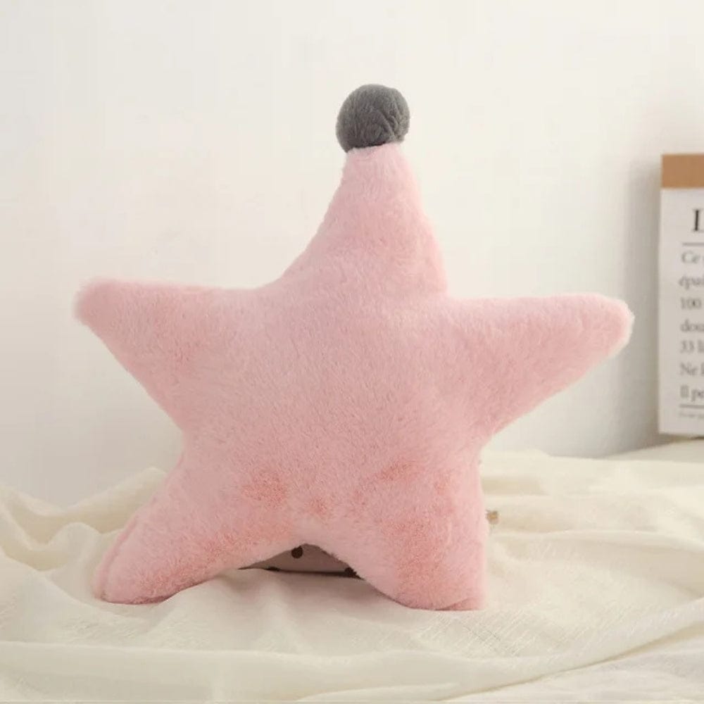 Coussin étoile rose en peluche avec une touche grise, posé sur un tissu doux dans une chambre