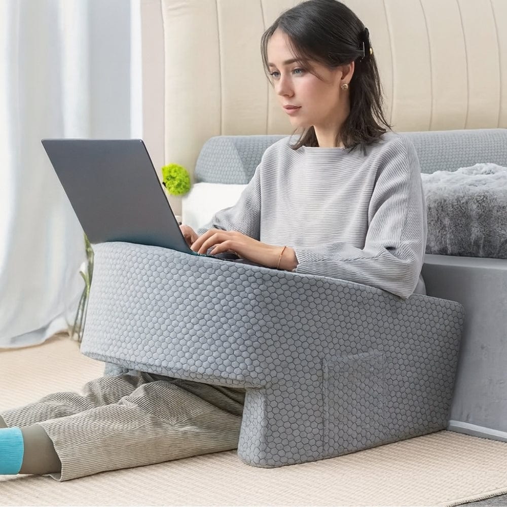 Coussin de soutien gris en forme de U, posé sur un tapis, avec une femme utilisant un ordinateur portable