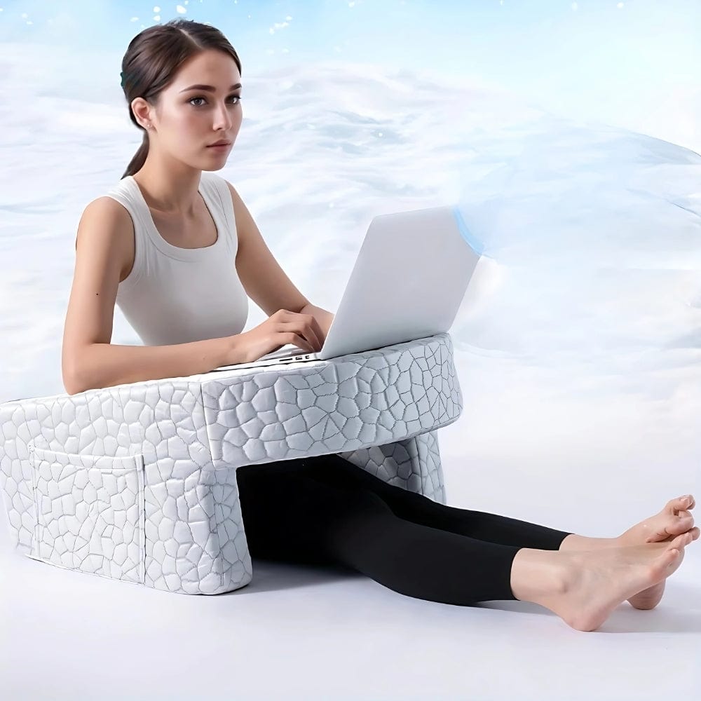 Coussin décoratif blanc en forme de support pour ordinateur portable, posé sur un sol clair avec une personne assise
