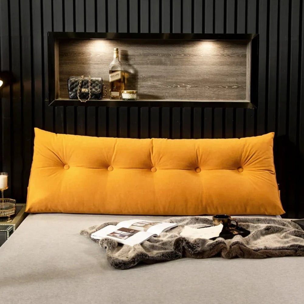 Coussin déco jaune moutarde en velours, placé sur un lit avec une couverture grise et des objets décoratifs