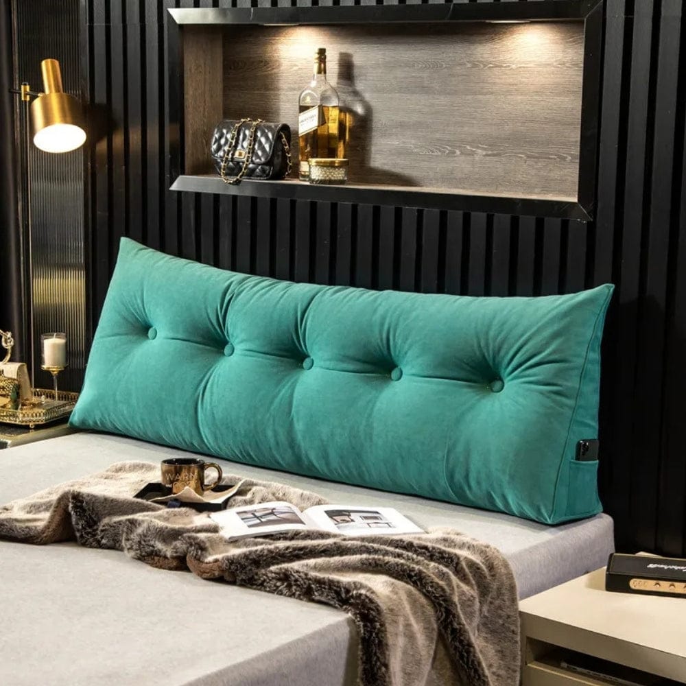 Coussin décoratif en velours vert turquoise, forme allongée avec boutons, posé sur un lit moderne avec une couverture douce