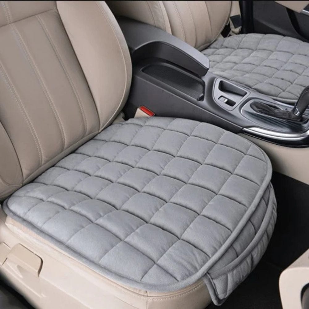 Coussin de voiture gris en tissu matelassé, posé sur un siège en cuir beige, offrant confort et style