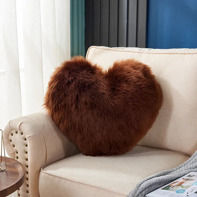 Coussin décoratif en forme de cœur, en moumoute marron, posé sur un canapé beige