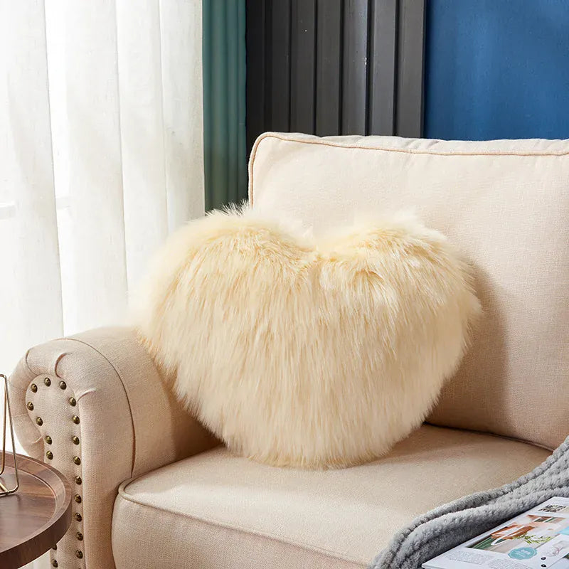 Coussin décoratif en forme de cœur, en moumoute beige, posé sur un canapé clair dans un salon élégant