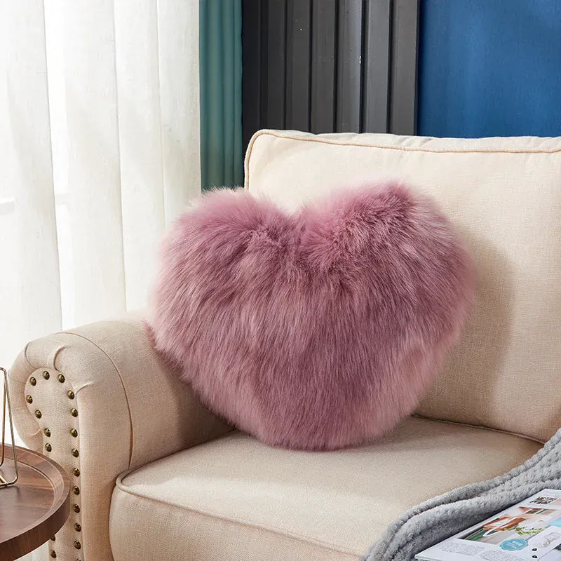 Coussin décoratif en forme de cœur, en moumoute rose, posé sur un canapé beige dans un salon moderne