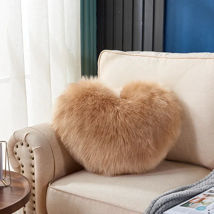 Coussin décoratif en moumoute beige en forme de cœur sur un canapé beige, ajoutant une touche chaleureuse au salon