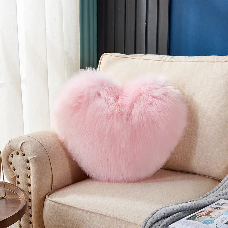 Coussin décoratif en forme de cœur, en moumoute rose, posé sur un canapé beige dans un salon lumineux