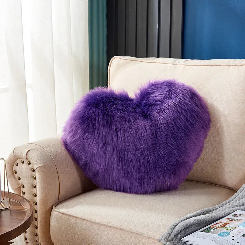 Coussin décoratif en forme de cœur, en moumoute violette, posé sur un canapé beige