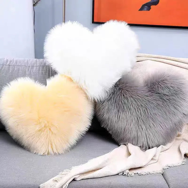 Coussins décoratifs en forme de cœur, en moumoute blanche, jaune et grise, sur un canapé gris