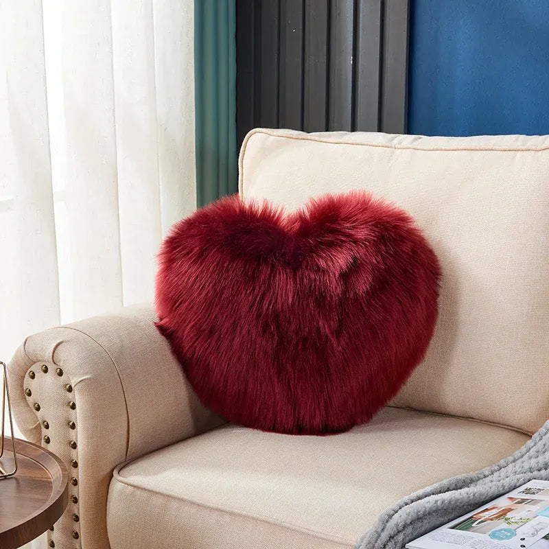 Coussin décoratif en forme de cœur, en moumoute rouge, posé sur un canapé beige élégant