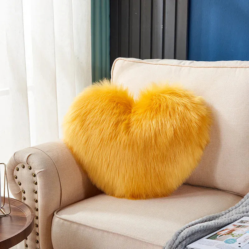 Coussin décoratif en forme de cœur, en moumoute jaune, posé sur un canapé beige dans un salon lumineux