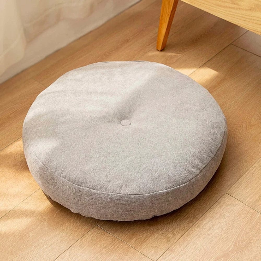 Coussin décoratif rond en tissu beige, posé sur un sol en bois, idéal pour un salon ou une chambre