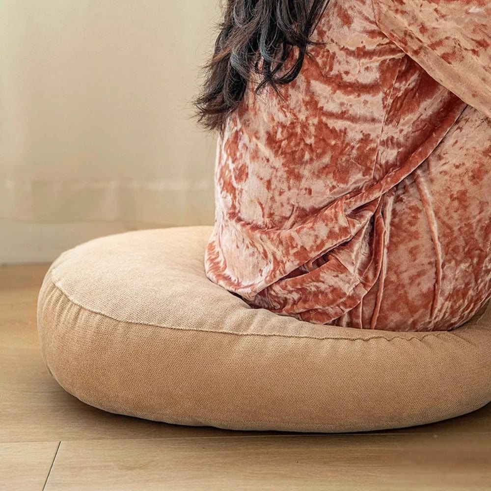 Gros coussin pouf rond en tissu beige, posé sur un sol en bois, offrant un confort moderne et chaleureux