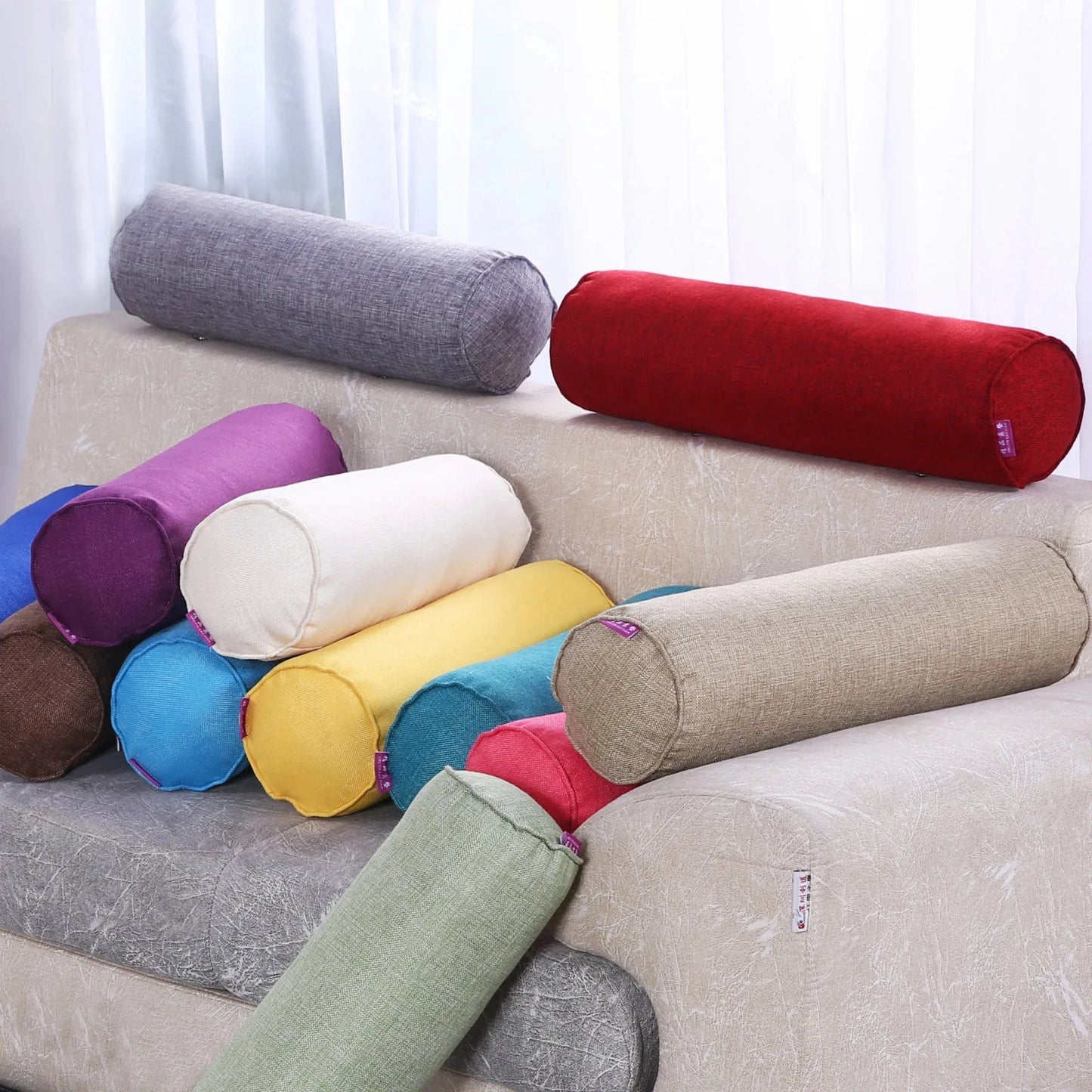 Coussins boudins colorés en tissu sur un canapé beige, ajoutant une touche décorative au salon