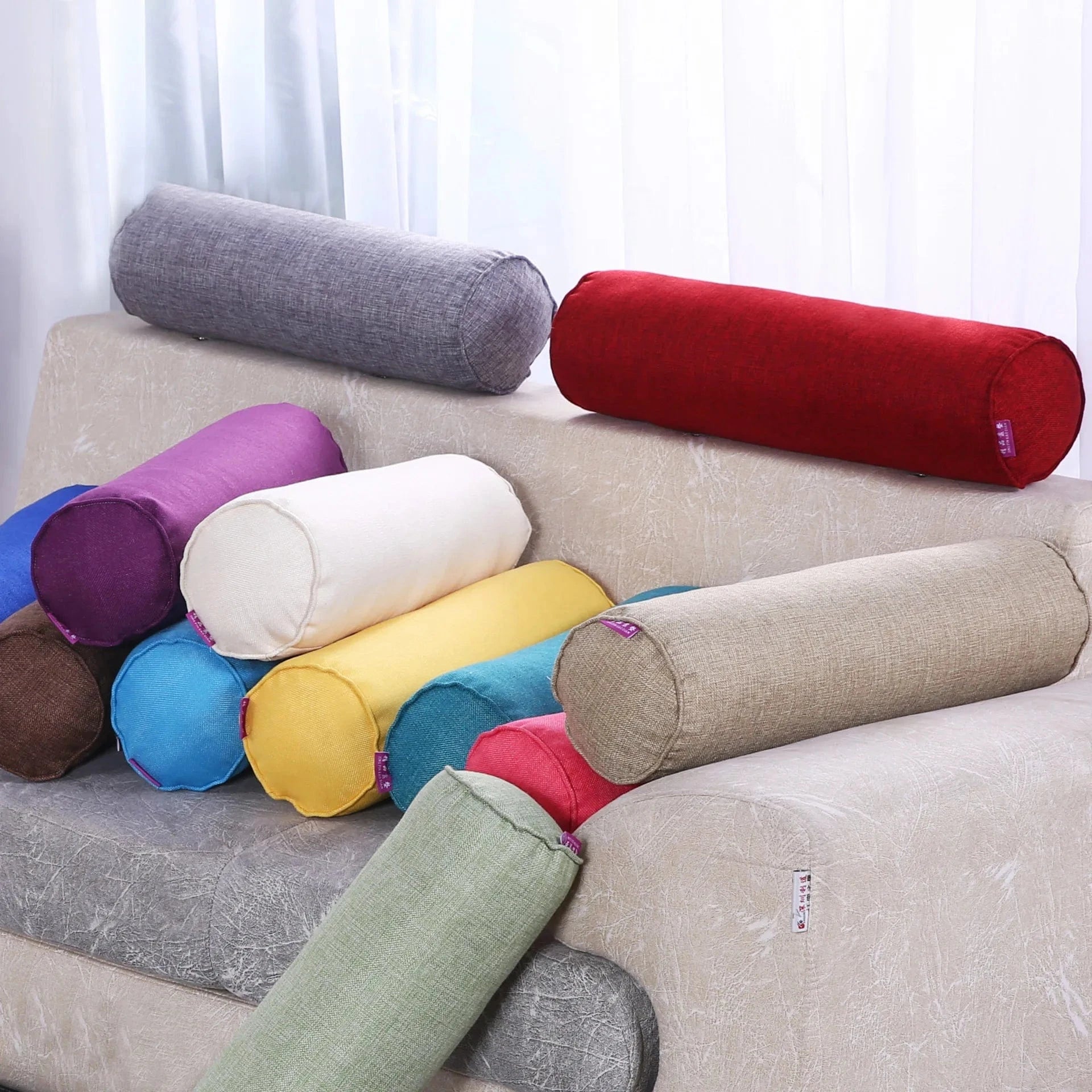 Coussins boudins colorés en tissu sur un canapé beige, ajoutant une touche décorative au salon