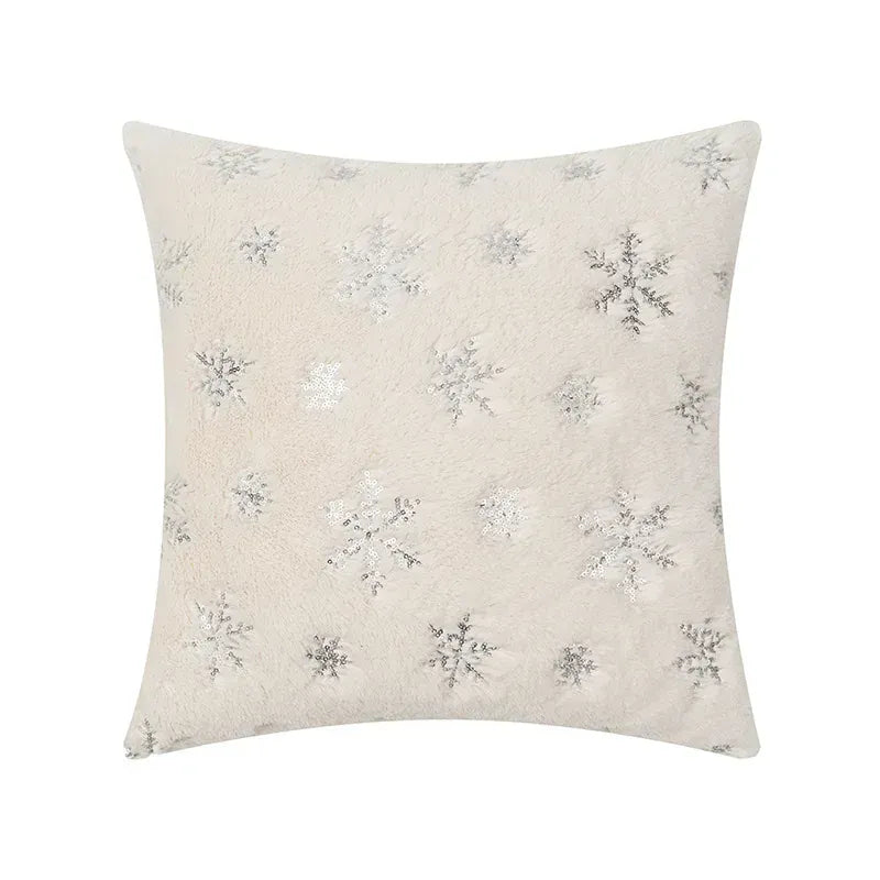 Coussin décoratif en tissu beige avec motifs flocons de neige argentés, posé sur un canapé moderne
