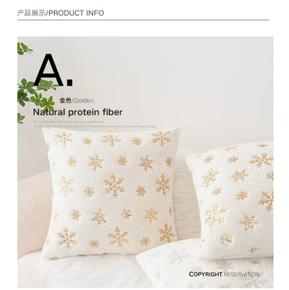 Coussin décoratif blanc avec motifs dorés de flocons de neige, posé sur un canapé en tissu doux