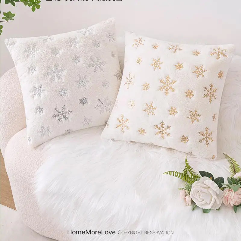 Coussins décoratifs en fausse fourrure blanche avec motifs flocons de neige argentés et dorés sur un canapé