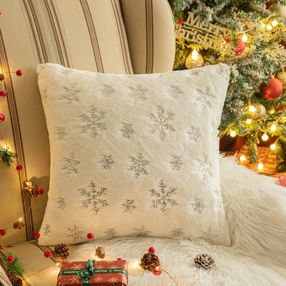 Coussin décoratif en fausse fourrure blanche avec motifs de flocons de neige sur un canapé cosy