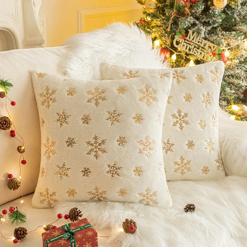 Coussins décoratifs aux motifs flocons de neige dorés sur fond crème, posés sur un canapé chaleureux