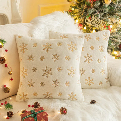 Coussins décoratifs aux motifs flocons de neige dorés sur fond crème, posés sur un canapé chaleureux