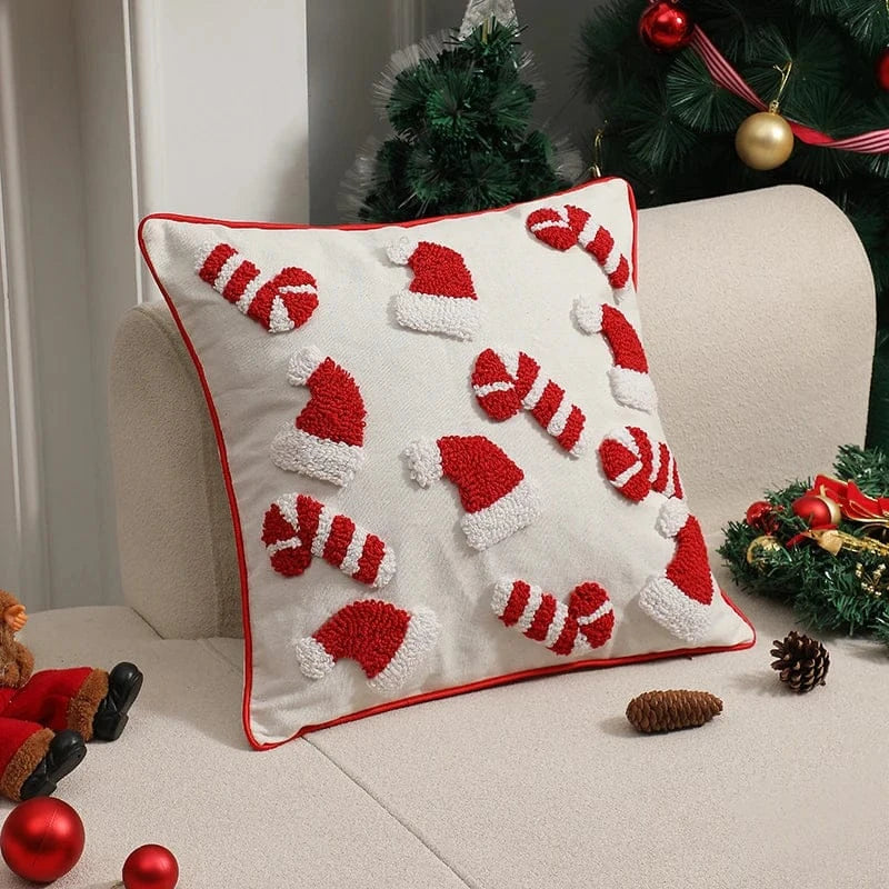 Coussin décoratif blanc avec motifs de bonnets de Noël rouges, posé sur un canapé beige, ajoutant une touche festive