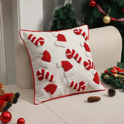 Coussin décoratif blanc avec motifs de bonnets de Noël rouges, posé sur un canapé beige, ajoutant une touche festive