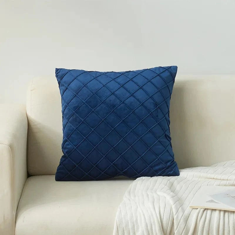 Coussin décoratif en velours bleu avec motif losanges, posé sur un canapé clair dans un salon moderne