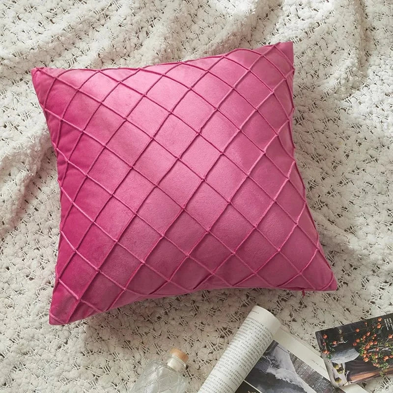 Coussin décoratif en velours rose avec motif en losanges, posé sur un plaid texturé dans un salon élégant