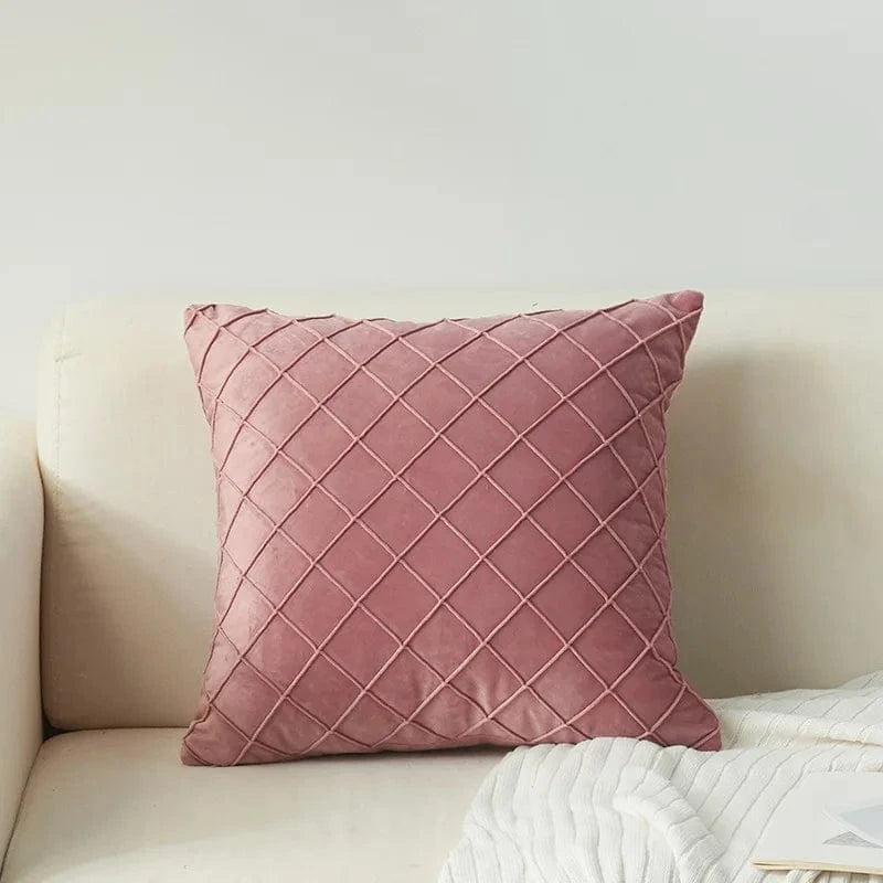 Coussin décoratif en velours rose avec motif en losanges, posé sur un canapé clair et élégant