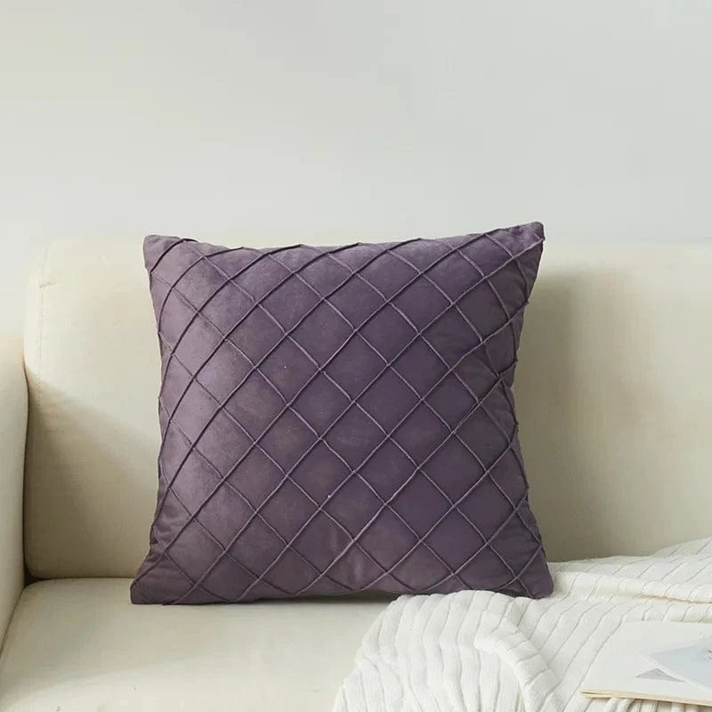 Coussin décoratif en velours violet avec motif losanges, posé sur un canapé clair dans un salon moderne