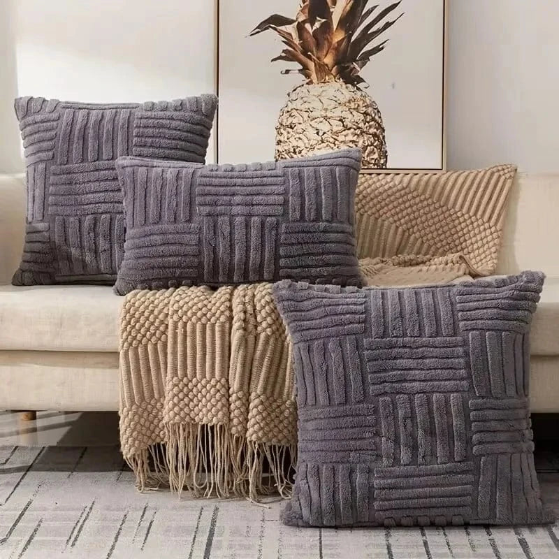 Coussins décoratifs en velours gris sur un canapé, avec des motifs texturés et un plaid beige en dessous
