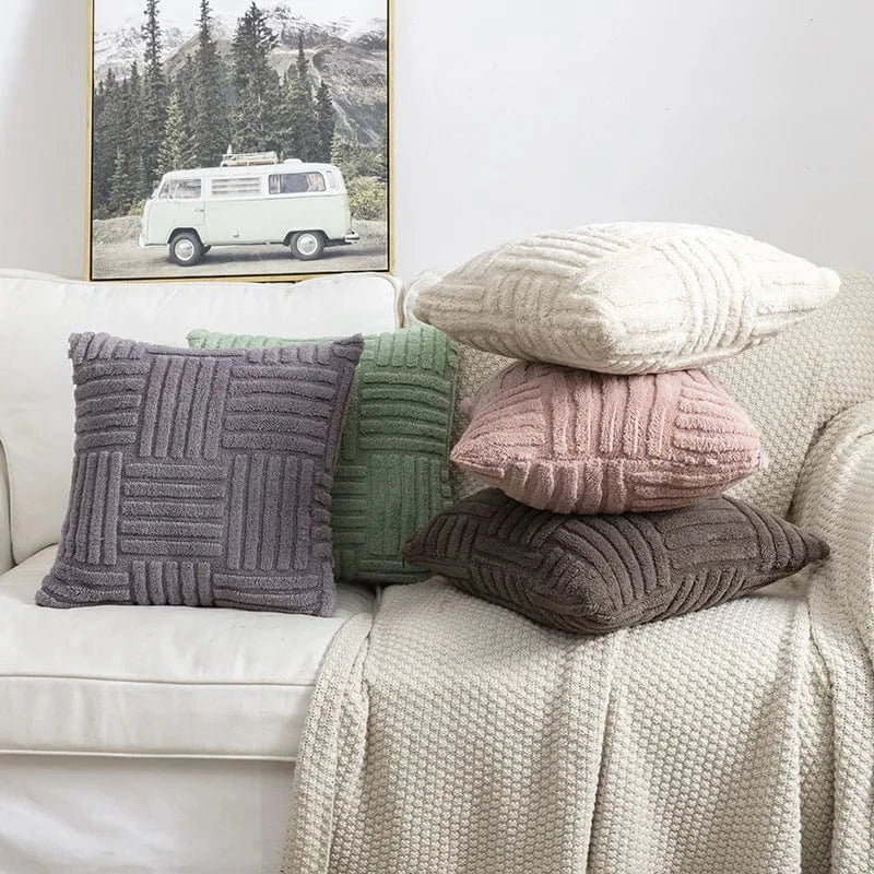 Coussins décoratifs aux textures variées, couleurs douces et motifs en relief, disposés sur un canapé beige