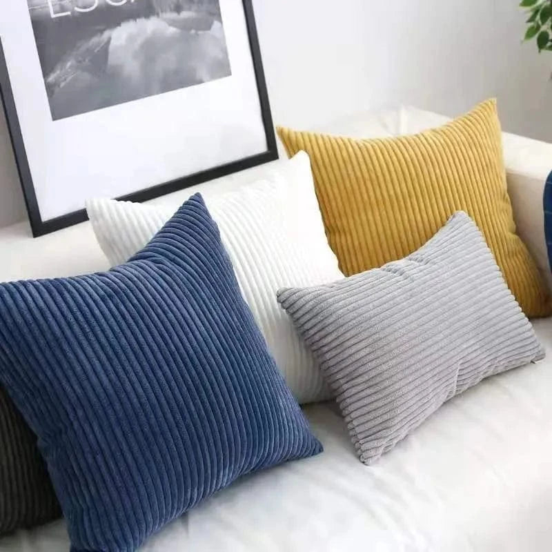 Coussins décoratifs en velours côtelé dans des teintes bleu, gris, blanc et jaune sur un canapé moderne
