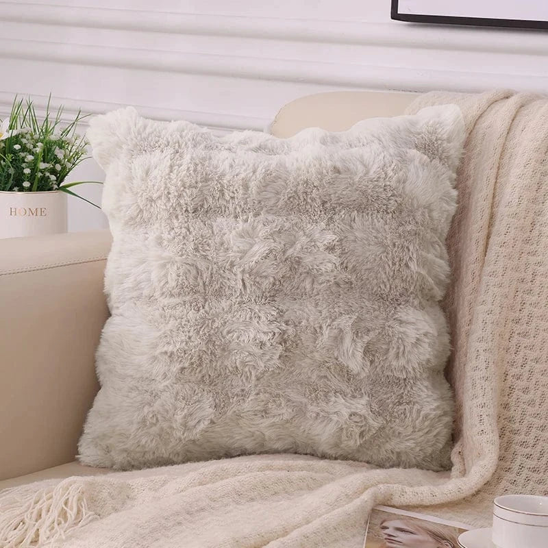 Coussin décoratif en fausse fourrure douce, couleur beige, posé sur un canapé avec un plaid et une plante