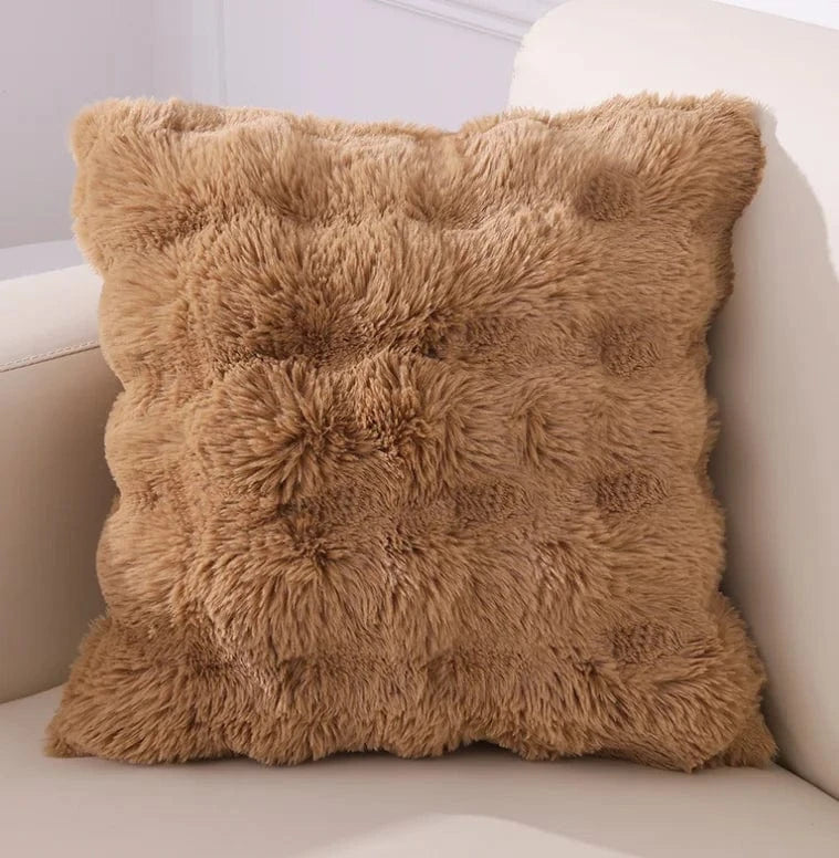 Coussin décoratif en fausse fourrure beige, doux et texturé, posé sur un canapé moderne pour un intérieur cocooning