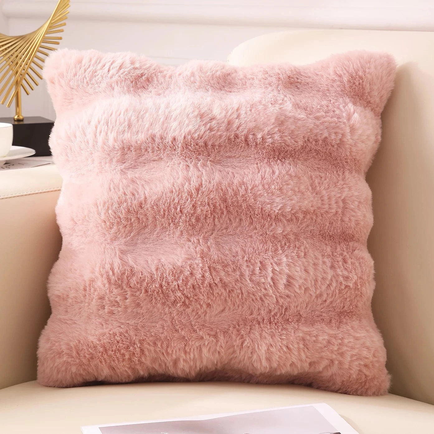 Coussin décoratif en fausse fourrure rose, posé sur un canapé, apportant une touche cocooning à l'intérieur