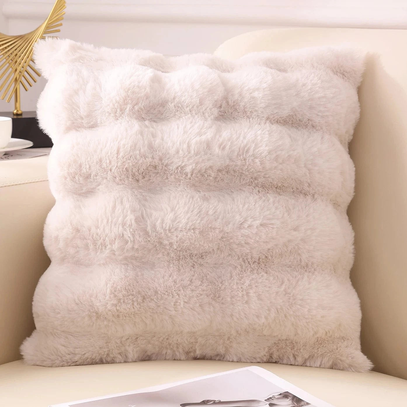 Coussin décoratif en fausse fourrure douce de couleur beige, posé sur un canapé clair, ajoutant une touche cocooning