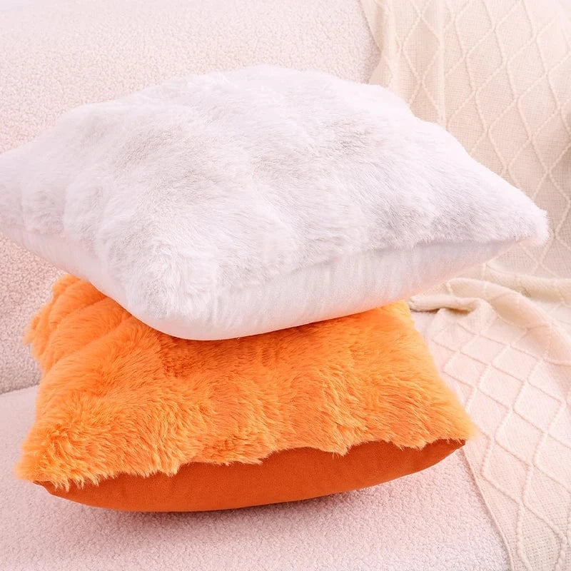 Coussins décoratifs en fausse fourrure blanche et orange posés sur un canapé beige, créant une ambiance cocooning